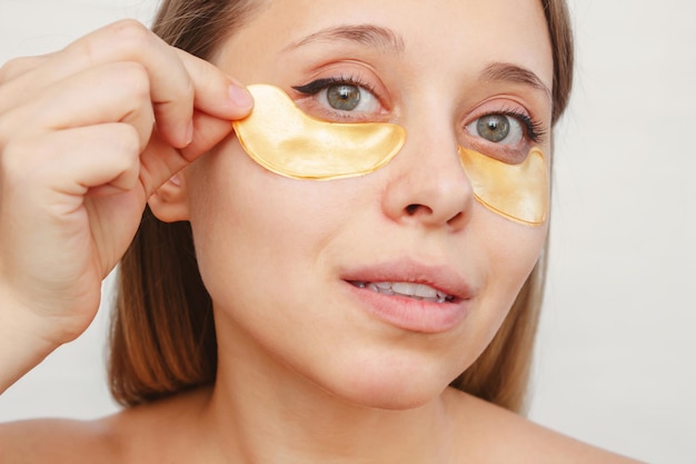 Una giovane donna mette dei cerotti dorati sulla pelle sotto gli occhi Cosmetologia per la cura della pelle