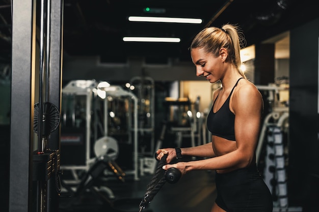 Una giovane donna muscolare sta facendo formazione sulla macchina in palestra. Sta pompando i muscoli delle braccia con un peso elevato.