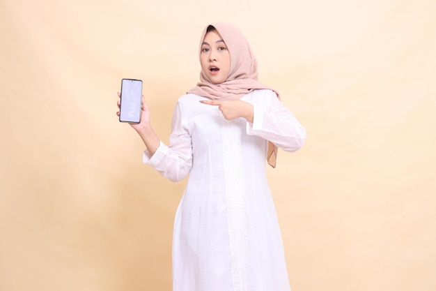 Una giovane donna musulmana asiatica che indossa un hijab è scioccata tenendo il suo gadget cellulare a destra in lei