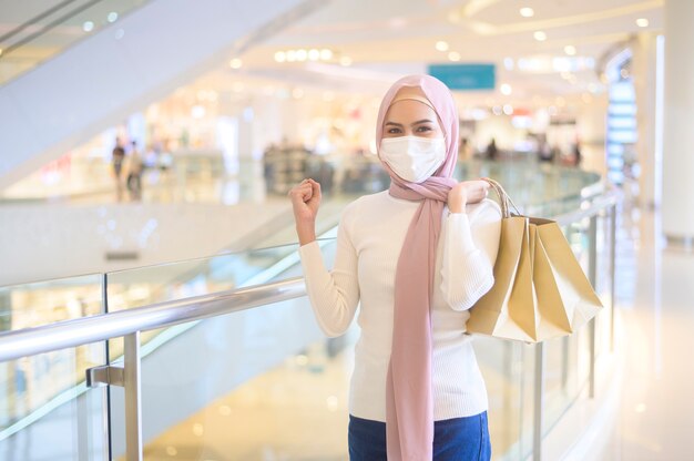 Una giovane donna musulmana che indossa una maschera protettiva nel centro commerciale, che fa shopping sotto il concetto di pandemia di Covid-19.