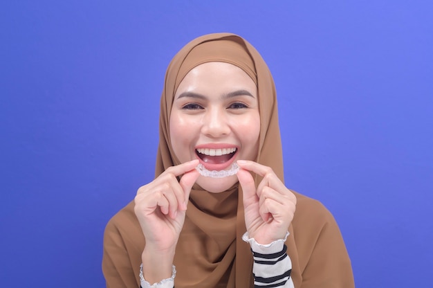 Una giovane donna musulmana che tiene bretelle invisalign in studio, assistenza sanitaria dentale e concetto ortodontico.