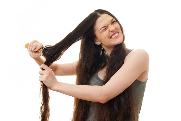 Una giovane donna non può pettinare i capelli aggrovigliati problematici. Su bianco isolato da vicino