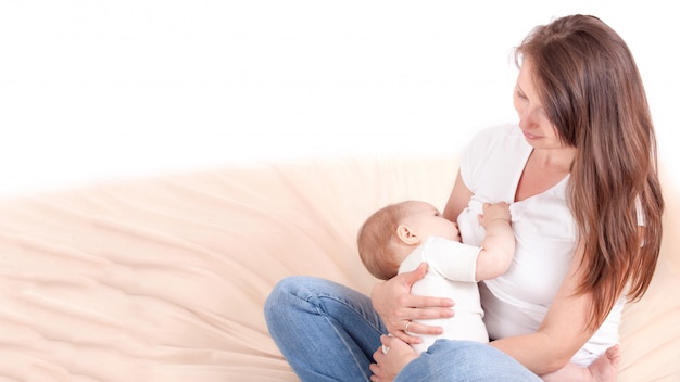 Una giovane donna nutre il petto del bambino, seduta sul letto. con spazio di testo libero.