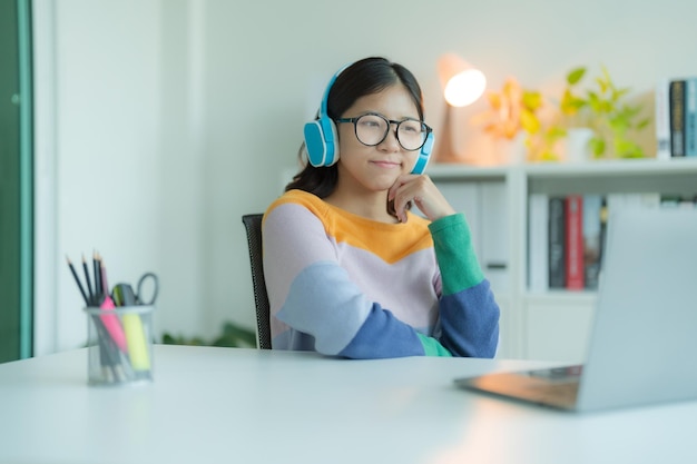 Una giovane donna o studente che utilizza un computer portatile in biblioteca mentre indossa occhiali e cuffie Sorride e sembra felice