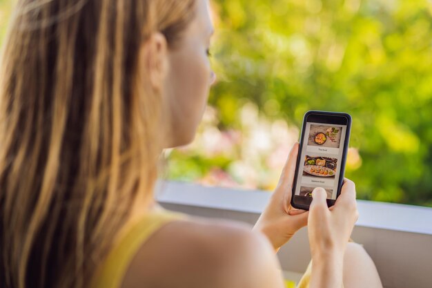 Una giovane donna ordina cibo per il pranzo online usando uno smartphone