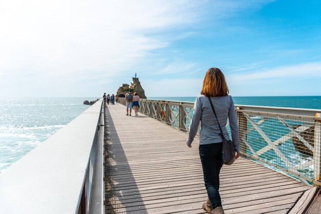 Una giovane donna passeggiando lungo il ponte di legno insieme a Plage du Port Vieux a Biarritz, in vacanza nel sud-est della Francia