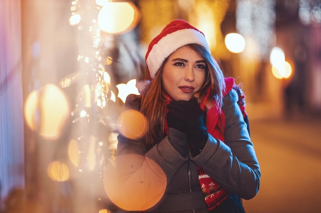 Una giovane donna pensierosa con una scatola regalo rossa sta aspettando qualcuno per la strada della città nel periodo natalizio.