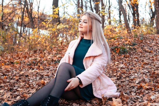 Una giovane donna piacevole in abiti casual con i capelli lunghi è seduta nella foresta autunnale