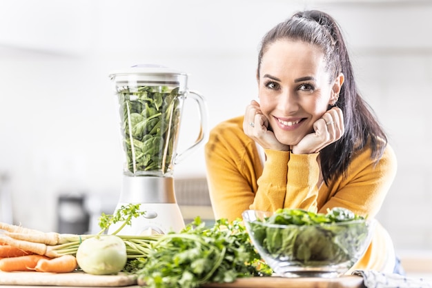 Una giovane donna prepara una bevanda energetica da verdure fresche utilizzando un frullatore