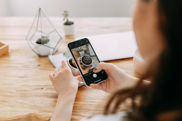 Una giovane donna scatta foto di oggetti beni cose usando un telefono cellulare crea contenuti per un blog