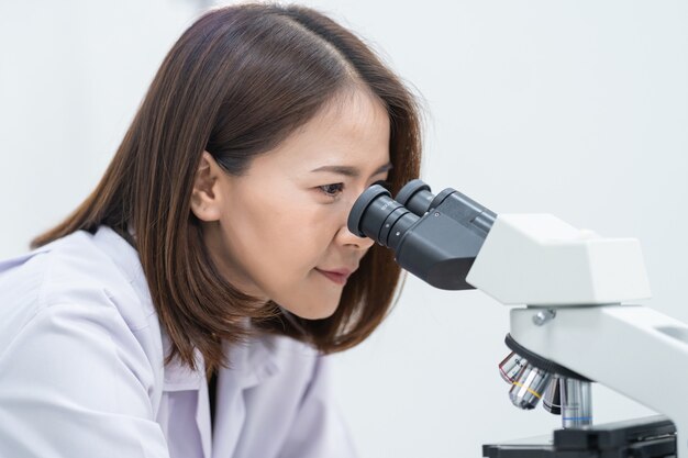 Una giovane donna scienziata in camice da laboratorio che guarda attraverso un microscopio in un laboratorio per fare ricerca e sperimentare. Scienziato che lavora in un laboratorio. Istruzione foto d'archivio