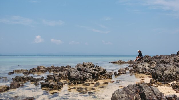 Una giovane donna seduta sulla roccia in riva al mare