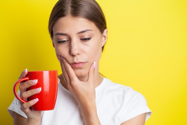 Una giovane donna sente mal di denti e tiene il posto del dolore con le mani