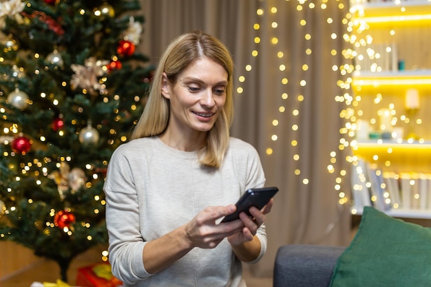 Una giovane donna si congratula per telefono con la famiglia e gli amici durante le vacanze di Natale che tiene in mano un