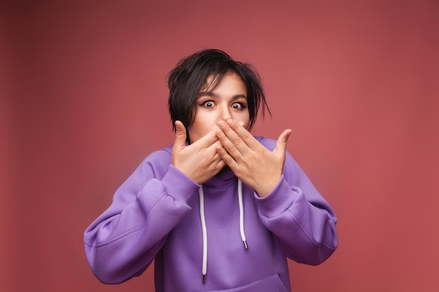 Una giovane donna si copre la bocca con la mano su uno sfondo rosa una donna con i capelli corti su uno sfondo rosa