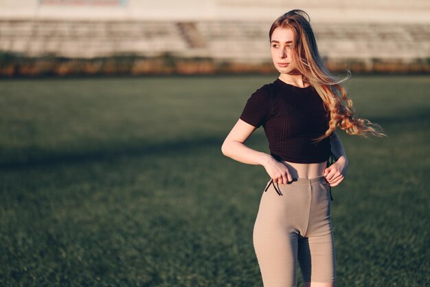 Una giovane donna si erge ai raggi del sole sullo sfondo di una ragazza di erba verde in abbigliamento sportivo