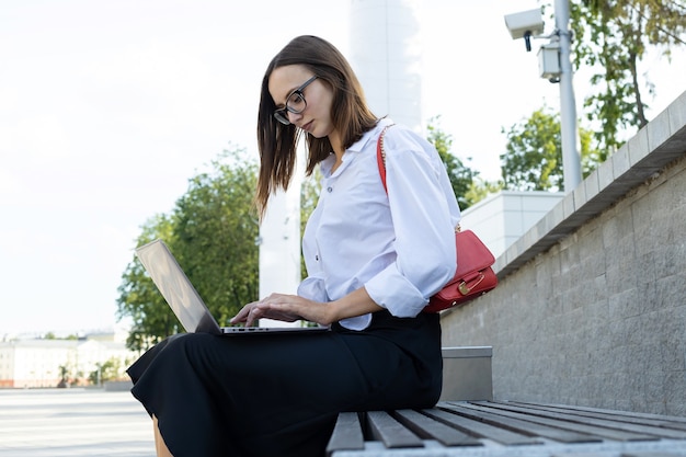 Una giovane donna si siede su una panchina e lavora a un laptop