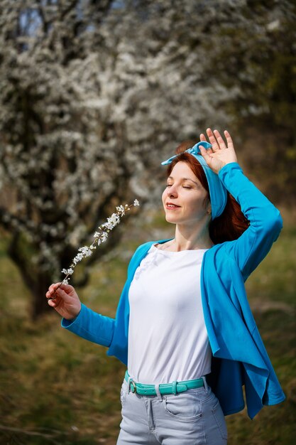 Una giovane donna si trova in un giardino dove fioriscono ciliegie e albicocche. È felice di respirare aria, fiori primaverili sullo sfondo