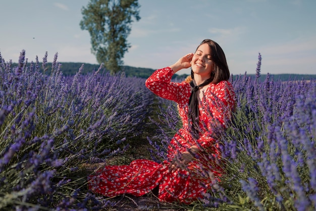 Una giovane donna siede in un campo di lavanda con un cappello di paglia appeso al collo