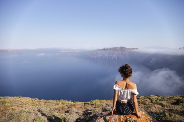 Una giovane donna siede sul bordo di una montagna e si gode il panorama