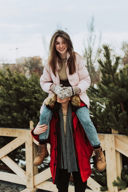 Una giovane donna siede sulle spalle di un uomo sullo sfondo degli alberi di Natale