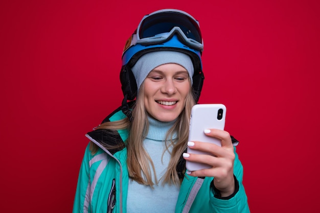 Una giovane donna snowboarder digita sul suo telefono su sfondo rosso