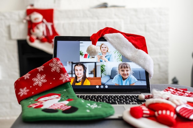 Una giovane donna sorridente che indossa il cappello rosso di Babbo Natale che fa videochiamata sui social network con la famiglia e gli amici il giorno di Natale.