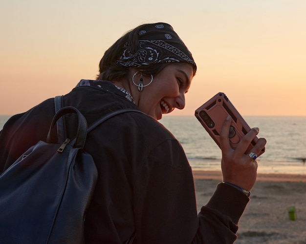 Una giovane donna sorridente che scatta una foto della telecamera al tramonto in riva al mare