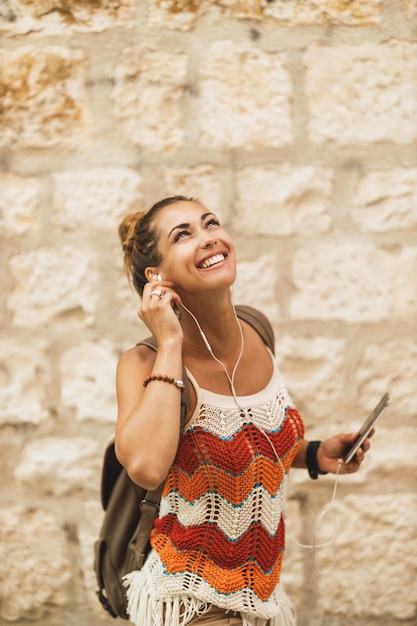 Una giovane donna sorridente che si gode la musica mentre esplora una città mediterranea durante una vacanza estiva.