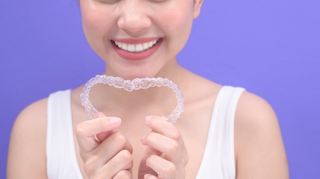 Una giovane donna sorridente che tiene bretelle invisalign in studio, assistenza sanitaria dentale e concetto ortodontico.