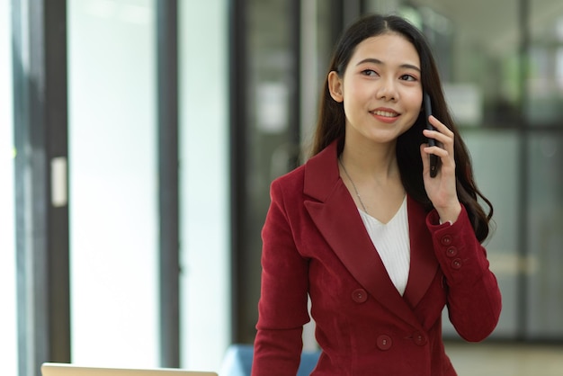 Una giovane donna sorridente che usa il telefono mentre è in piedi contro il muro