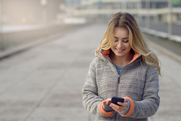 Una giovane donna sorridente con i capelli biondi che usa il telefono mentre è in piedi sul ponte