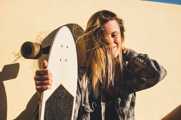 Una giovane donna sorridente con uno skateboard seduta contro un muro di sostegno in una giornata di sole