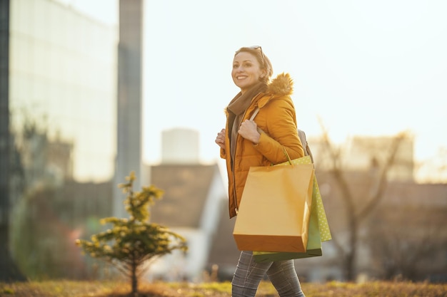 Una giovane donna sorridente felice sta camminando in città con le borse della spesa.