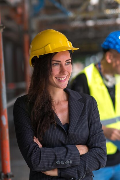 Una giovane donna sorridente, manager di costruzione o ingegnere, posa con le braccia incrociate e guarda da un'altra parte.