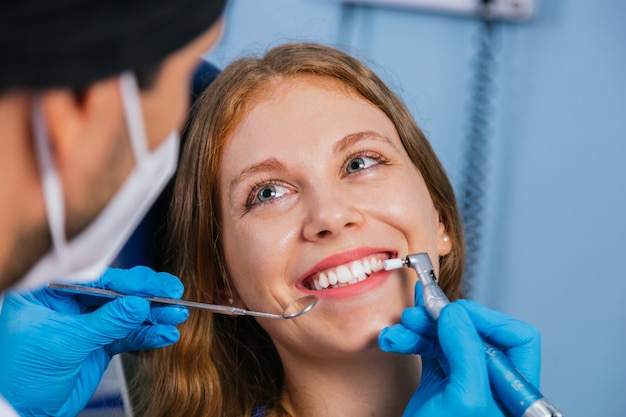Una giovane donna sorridente si siede su una sedia da dentisti mentre il medico le esamina i denti