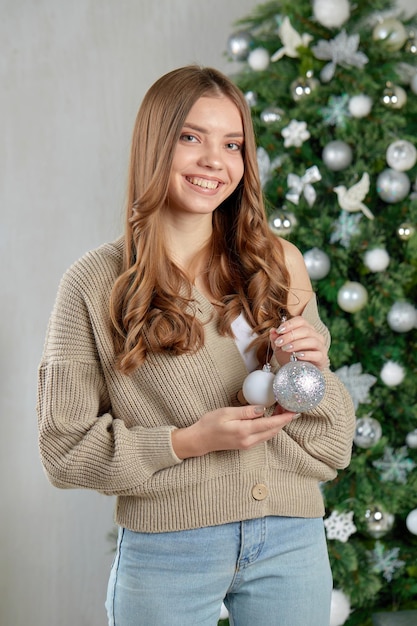 Una giovane donna sorridente si trova all'albero di Natale con i giocattoli di Natale nelle sue mani