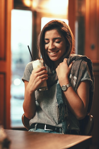 Una giovane donna sorridente sta bevendo caffè con panna montata mentre è seduta al bar.