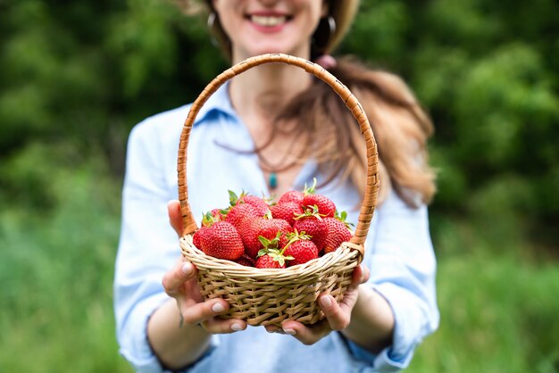 Una giovane donna sorridente tiene in mano un cesto con fragole mature.