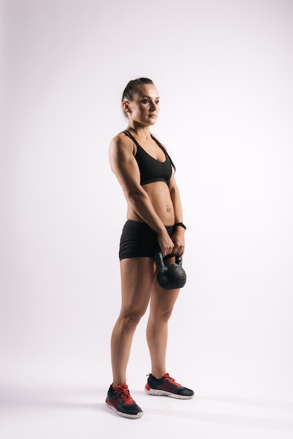 Una giovane donna sportiva con un corpo muscoloso perfetto è in piedi con un kettlebell da kg