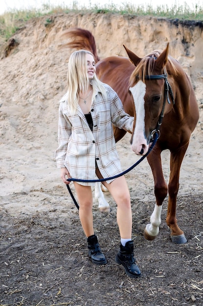 Una giovane donna sta con il suo cavallo in natura e sorride Foto a figura intera al pascolo di un cavallo