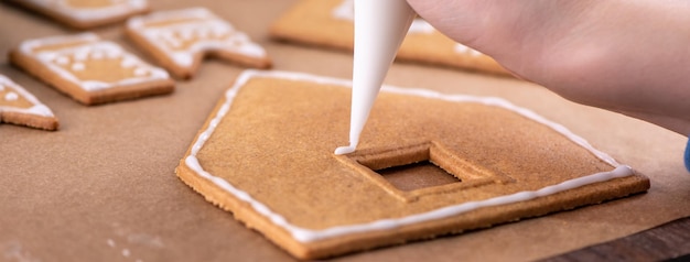 Una giovane donna sta decorando il biscotto di Natale Gingerbread House biscotto a casa con glassa in borsa di glassa stile di vita ravvicinato