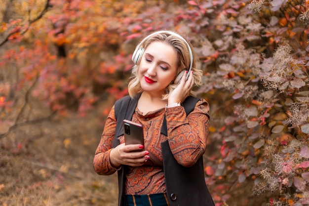 Una giovane donna sullo sfondo di un parco autunnale con le cuffie che ascolta la musica