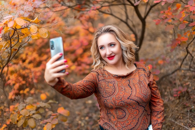 Una giovane donna sullo sfondo di un parco autunnale si fa un selfie con il telefono