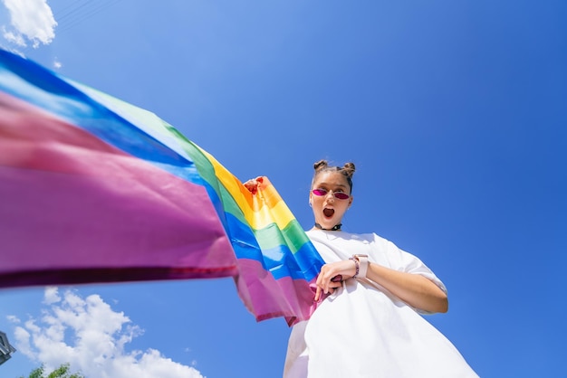 Una giovane donna sviluppa una bandiera arcobaleno contro il cielo