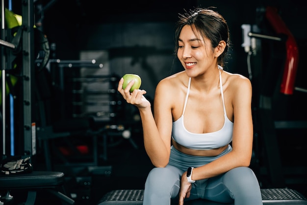 Una giovane donna tiene in mano una mela verde in palestra, ricordando agli spettatori l'importanza di una dieta equilibrata per raggiungere gli obiettivi di fitness. Concetto di fitness sano e stile di vita alimentare