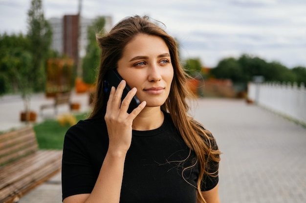 Una giovane donna tranquilla e calma sta chiamando qualcuno al telefono mentre cammina