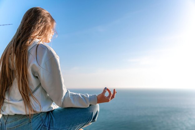 Una giovane donna turistica che si gode il tramonto sul paesaggio di montagna del mare mentre si siede yoga all'aperto delle donne