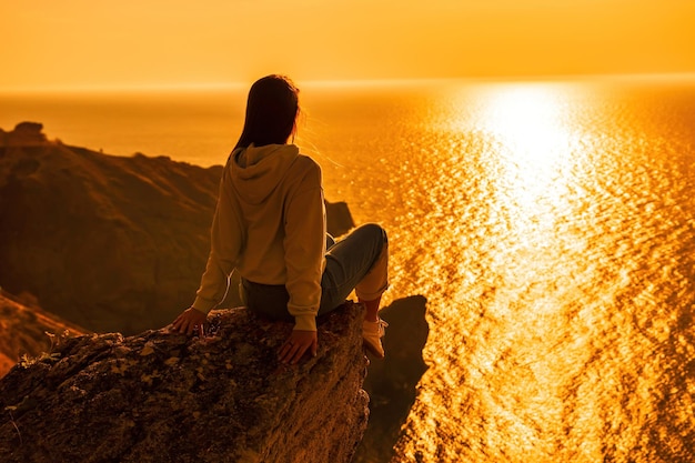 Una giovane donna turistica che si gode il tramonto sul paesaggio montano del mare mentre è seduta all'aperto per lo yoga delle donne