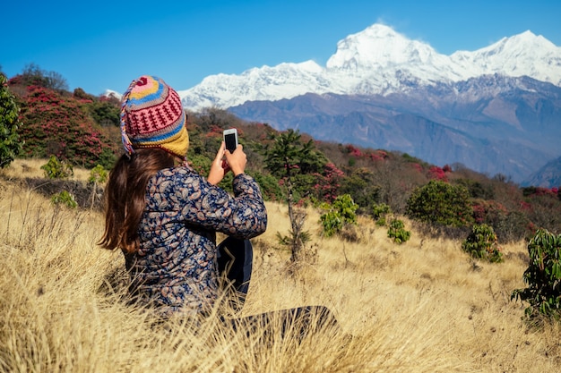 Una giovane donna turistica con uno zaino da trekking e un cappello a maglia che fotografa i paesaggi e si fa selfie nelle montagne dell'Himalaya. concetto di trekking in montagna